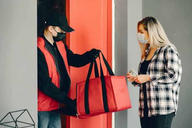 Masked delivery man handing a woman her order